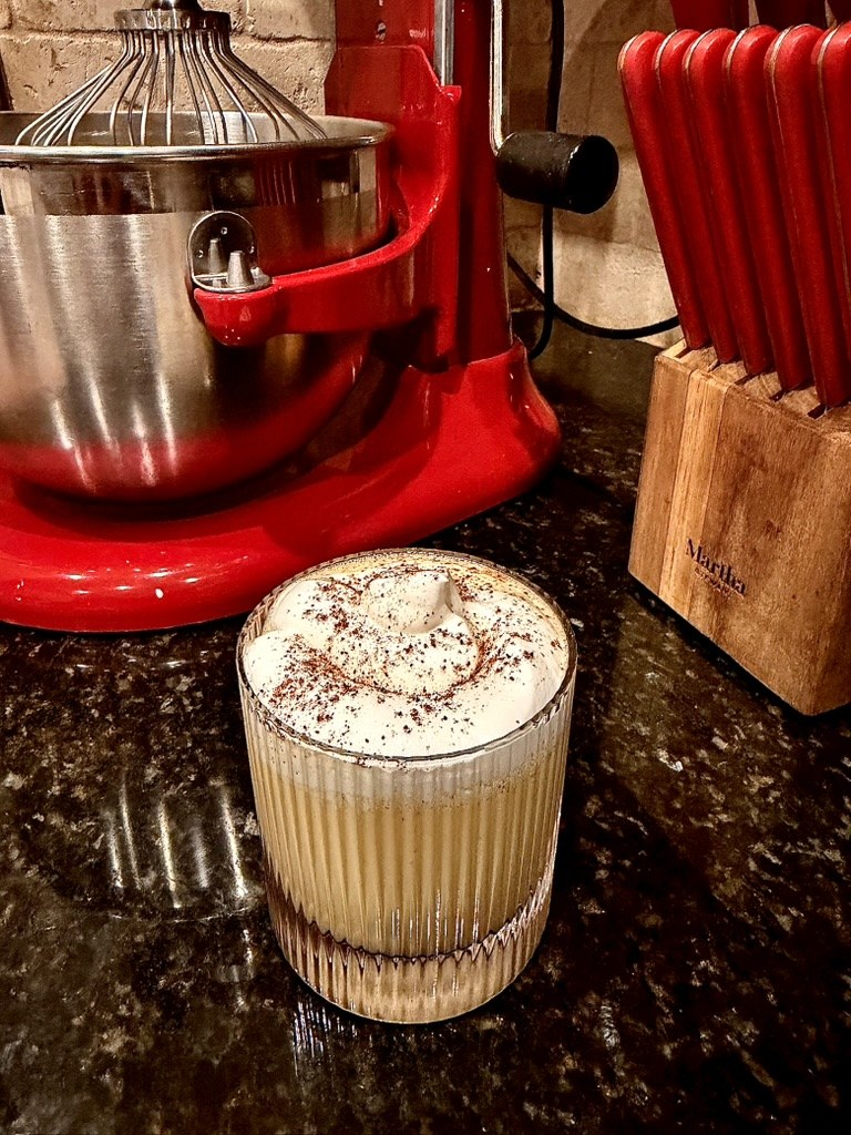 A festive eggnog presented in a ribbed glass with whipped topping and nutmeg.