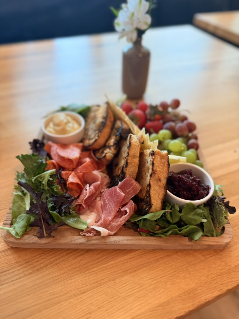 Charcuterie board with cured meats, artisan cheeses, grilled sourdough, fruit, mustard, blackberry jam, and spring mix.