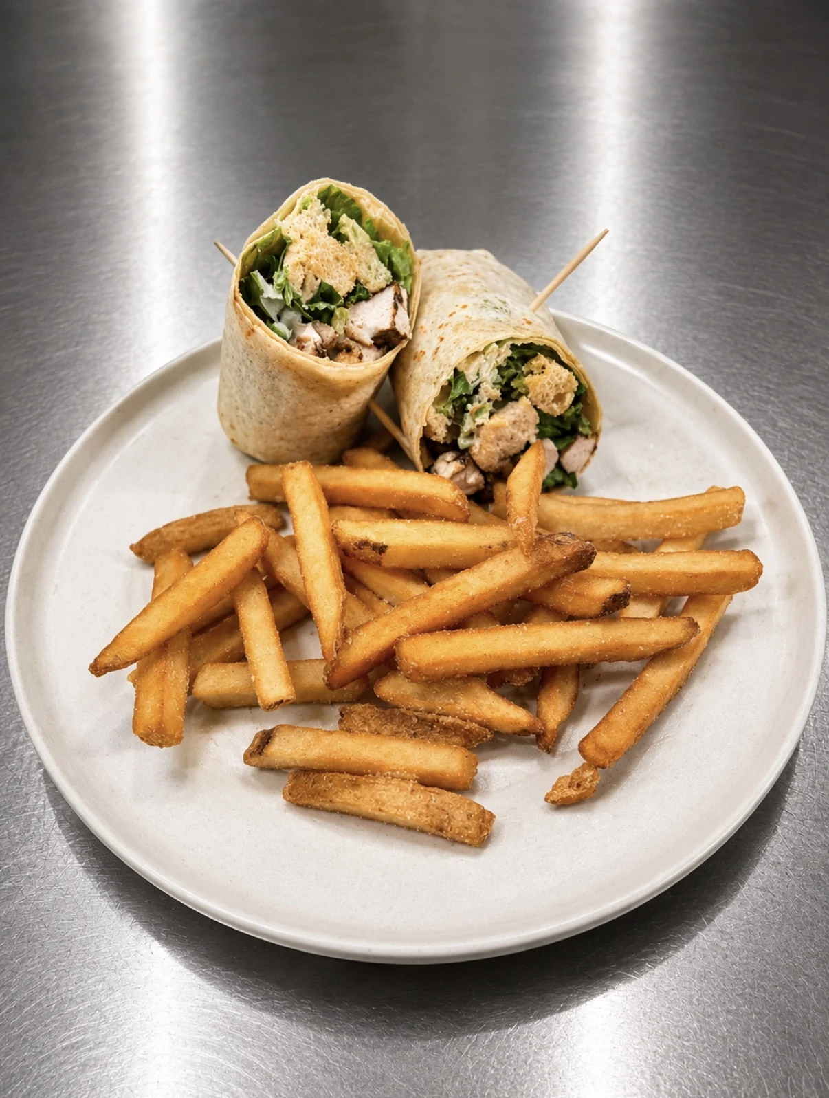 Chicken Caesar wrap cut in halves and served with seasoned fries.