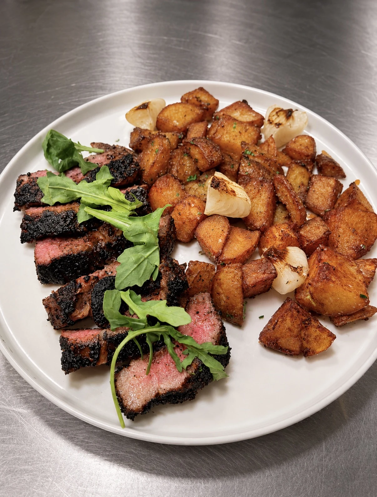 Sliced cowboy-rubbed New York strip with roasted potatoes, grilled onions, and arugula.