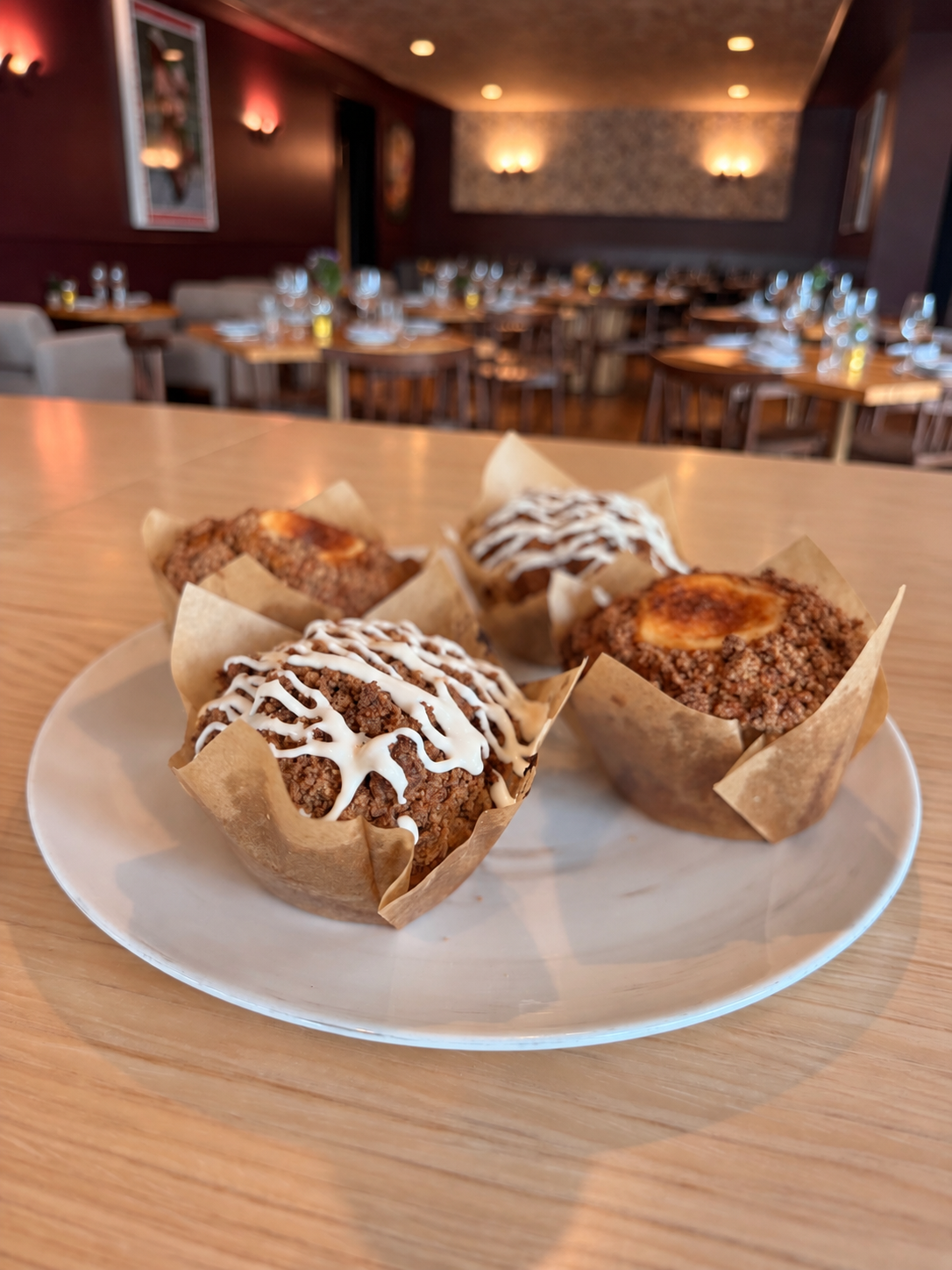 Four pumpkin spice muffins on a white plate, two drizzled with cinnamon cream cheese icing and two with vanilla cream cheese filling.